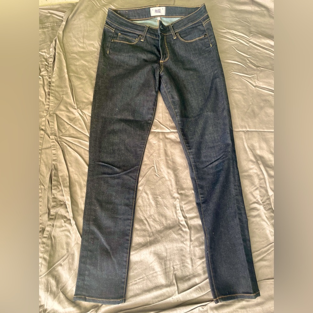 PAIGE  dark denim jeans with yellowish stitching.